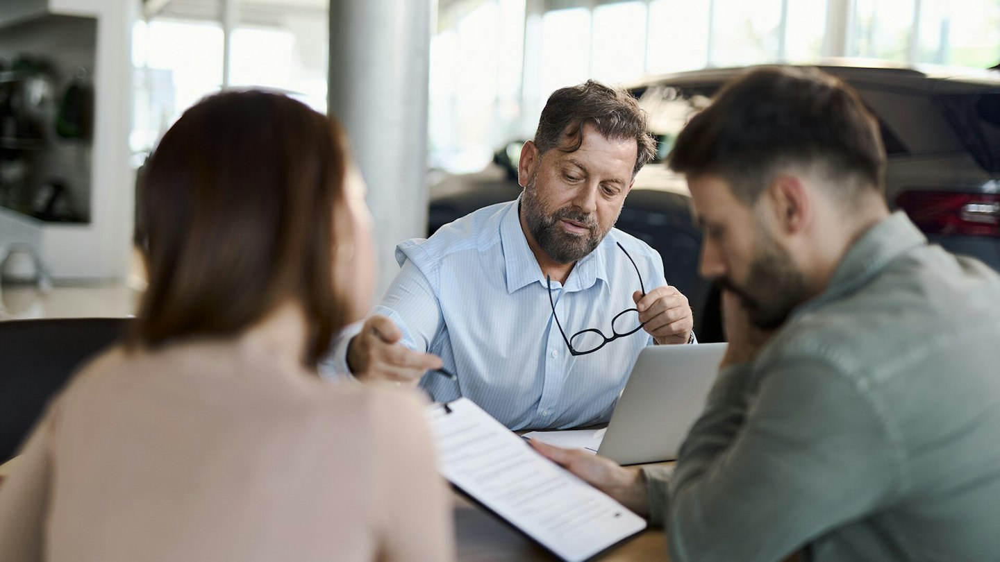 Un vendeur de voitures explique un contrat à un couple.